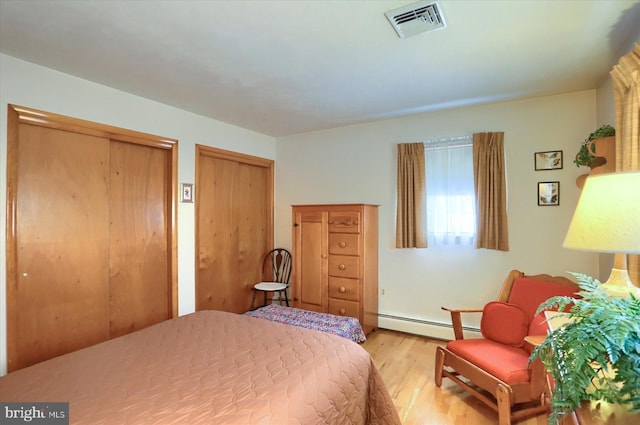 bedroom featuring baseboard heating, multiple closets, and light wood-type flooring