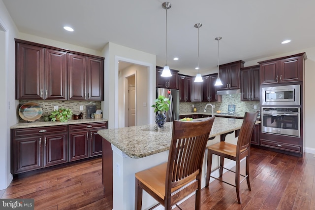 kitchen with light stone counters, decorative light fixtures, dark hardwood / wood-style flooring, an island with sink, and stainless steel appliances