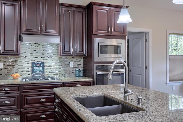 kitchen with appliances with stainless steel finishes, decorative light fixtures, sink, backsplash, and light stone countertops