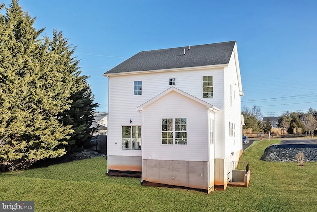 rear view of house featuring a shingled roof and a yard