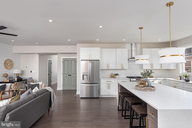 kitchen featuring stainless steel refrigerator with ice dispenser, light countertops, backsplash, open floor plan, and wall chimney range hood