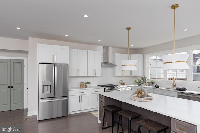 kitchen featuring light countertops, appliances with stainless steel finishes, white cabinetry, a sink, and wall chimney exhaust hood