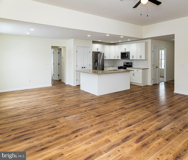 kitchen featuring light stone counters, wood-type flooring, a center island, stainless steel appliances, and white cabinets