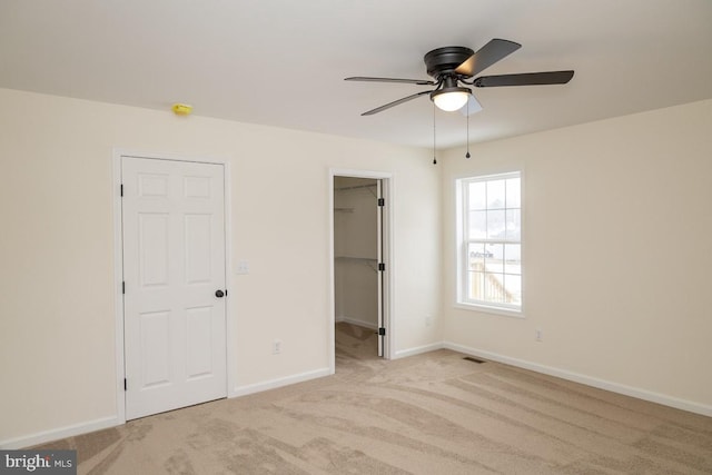 unfurnished bedroom featuring a spacious closet, light carpet, ceiling fan, and a closet