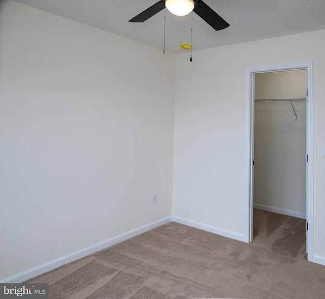 unfurnished bedroom featuring a walk in closet, light carpet, ceiling fan, and a closet