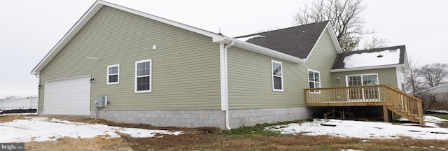 snow covered property with a wooden deck and a garage