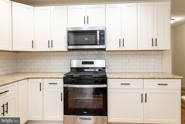 kitchen featuring white cabinetry, stainless steel appliances, light stone countertops, and backsplash