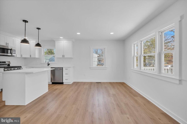 kitchen featuring white cabinetry, decorative light fixtures, stainless steel appliances, and light hardwood / wood-style floors