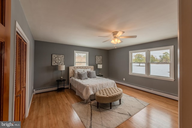 bedroom with a closet, ceiling fan, baseboard heating, and light hardwood / wood-style flooring