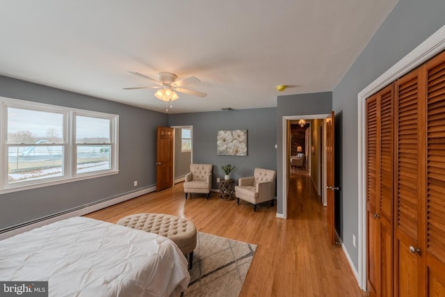 bedroom with light wood-type flooring, a closet, ceiling fan, and baseboard heating