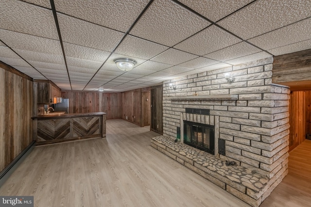 bar featuring stainless steel refrigerator, a fireplace, wooden walls, and light hardwood / wood-style flooring