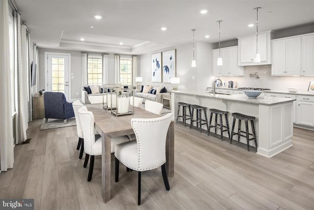 dining area with sink, light hardwood / wood-style floors, and a raised ceiling