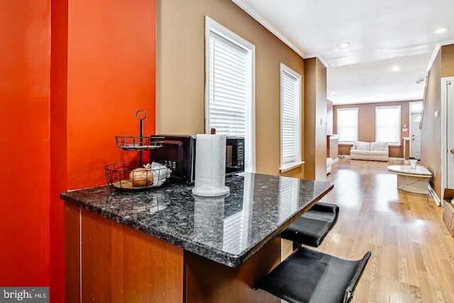 interior space featuring ornamental molding, light hardwood / wood-style flooring, and dark stone counters