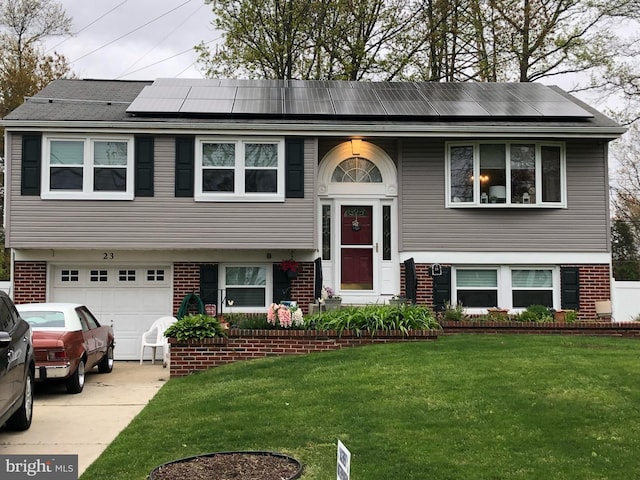 bi-level home featuring a garage, a front lawn, and solar panels