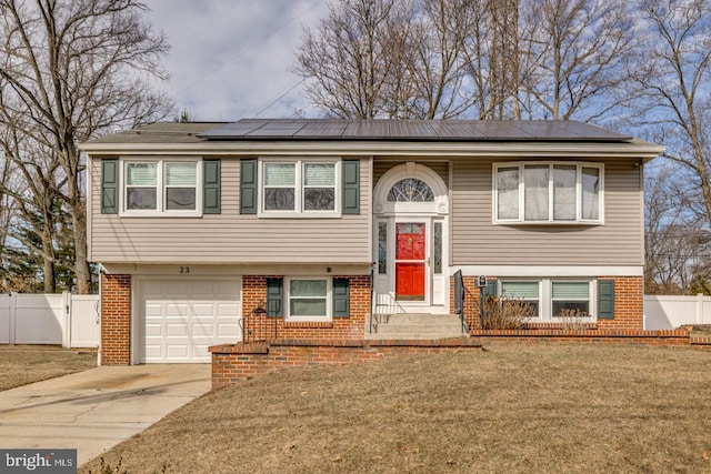 split foyer home featuring solar panels, brick siding, fence, driveway, and a front lawn