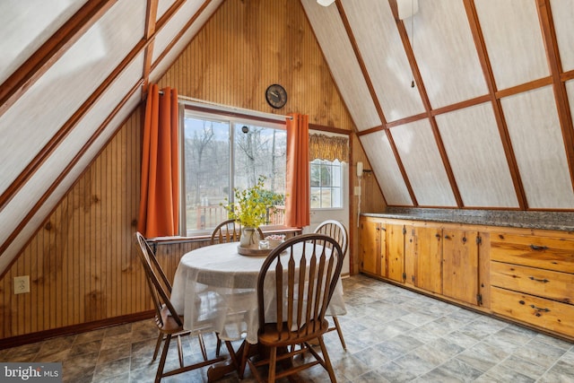 dining area with vaulted ceiling, stone finish floor, baseboards, and wooden walls