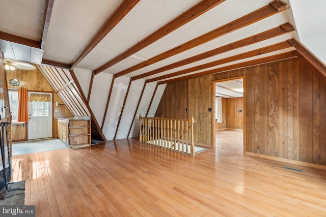 additional living space featuring hardwood / wood-style flooring, wooden walls, visible vents, and beamed ceiling