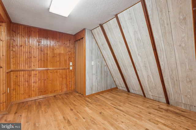 additional living space featuring a textured ceiling, hardwood / wood-style floors, wood walls, and baseboards