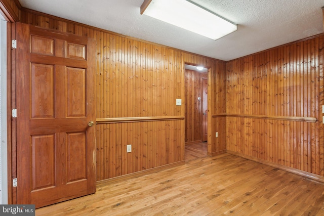 spare room featuring wood-type flooring, wooden walls, and baseboards