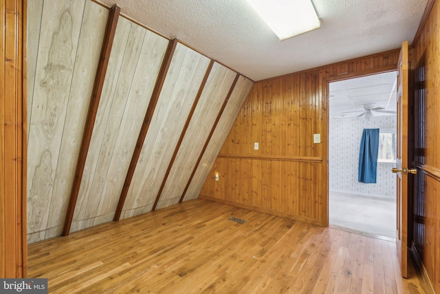 bonus room with wooden walls, wood-type flooring, and a textured ceiling