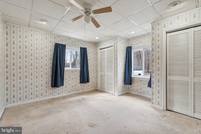 unfurnished bedroom with wallpapered walls, carpet, baseboards, and two closets