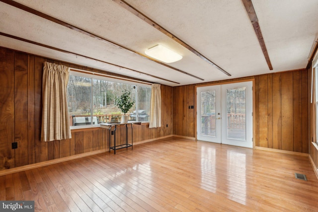 spare room with wood walls, wood-type flooring, visible vents, and french doors