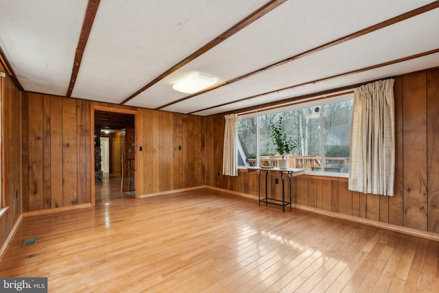 spare room featuring baseboards, wood-type flooring, visible vents, and wooden walls