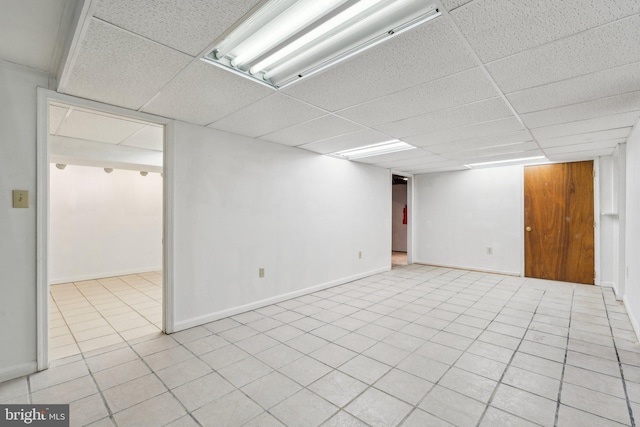 finished basement featuring light tile patterned floors, a drop ceiling, and baseboards