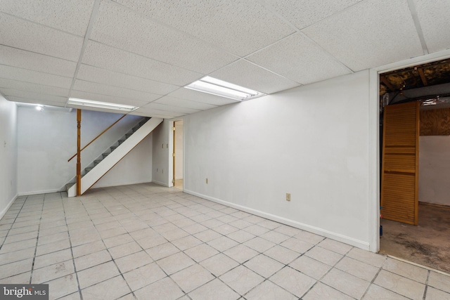 finished basement with light tile patterned floors, stairway, a paneled ceiling, and baseboards