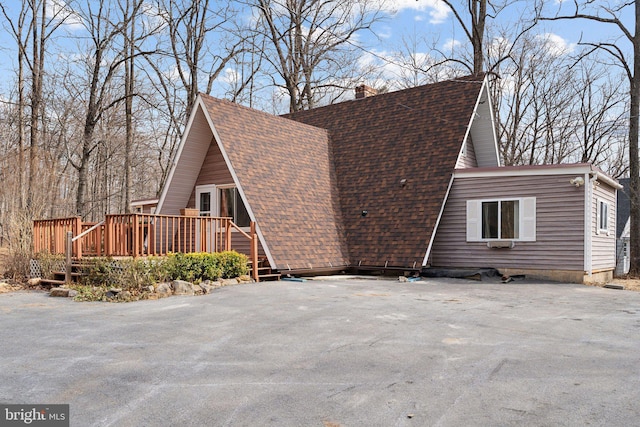 view of side of property featuring roof with shingles, a chimney, and a wooden deck