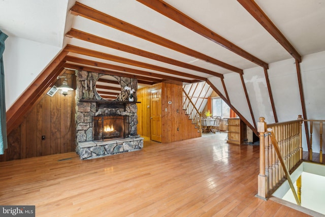 additional living space with vaulted ceiling with beams, a fireplace, stairway, wooden walls, and hardwood / wood-style floors