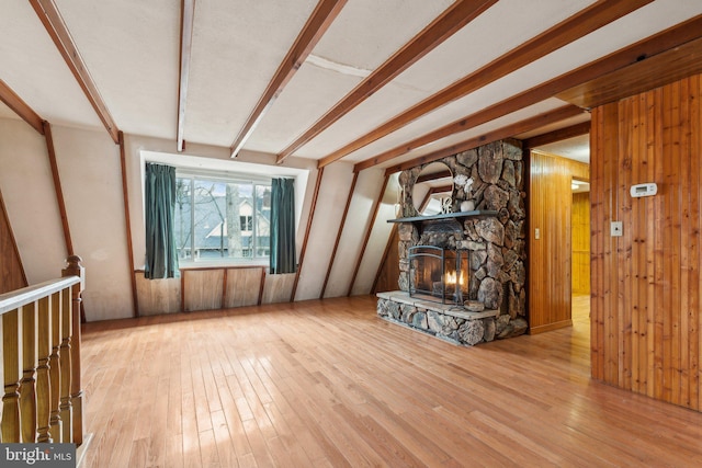 unfurnished living room featuring hardwood / wood-style floors, a fireplace, beam ceiling, and wooden walls