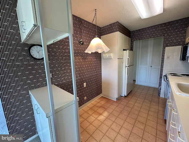 kitchen with white refrigerator, white cabinetry, decorative light fixtures, and a textured ceiling