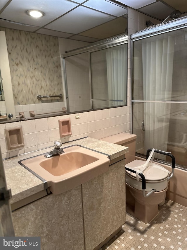 full bathroom featuring bath / shower combo with glass door, sink, tile walls, and toilet