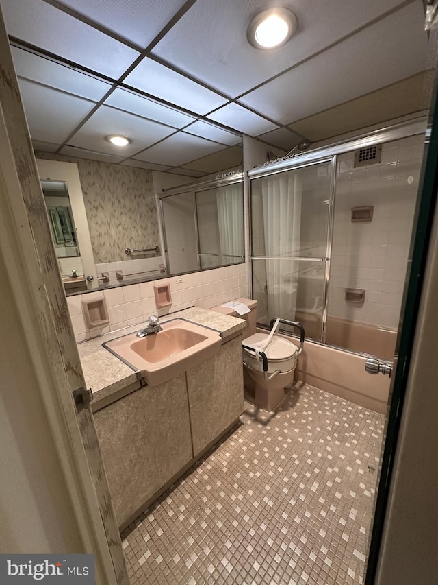 full bathroom featuring vanity, bath / shower combo with glass door, toilet, and a paneled ceiling