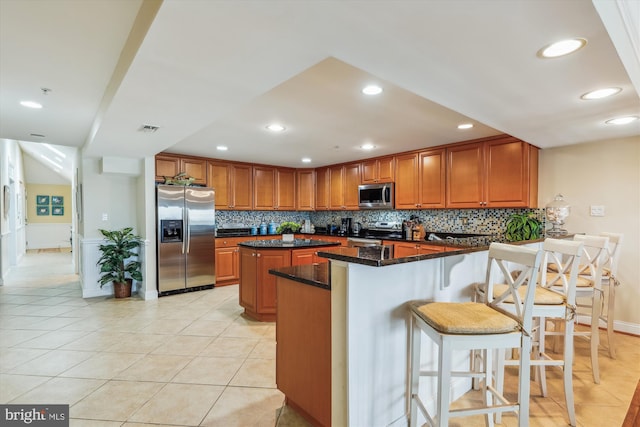 kitchen featuring a kitchen island, appliances with stainless steel finishes, decorative backsplash, dark stone counters, and light tile patterned floors