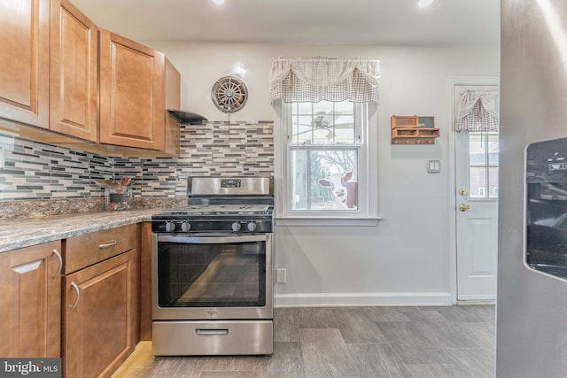 kitchen featuring gas range, backsplash, and light stone counters