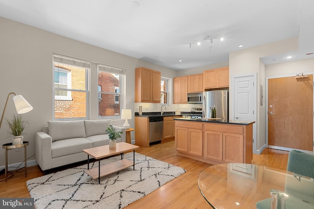 kitchen featuring appliances with stainless steel finishes, light brown cabinetry, sink, a center island, and light hardwood / wood-style flooring