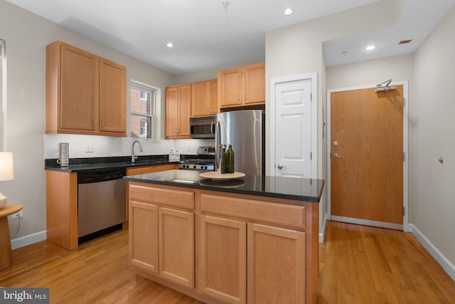 kitchen with sink, tasteful backsplash, a kitchen island, stainless steel appliances, and light hardwood / wood-style floors