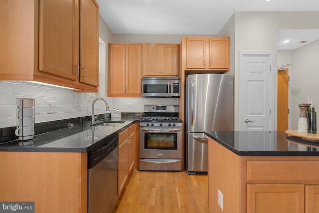 kitchen with sink, dark stone countertops, light wood-type flooring, appliances with stainless steel finishes, and decorative backsplash