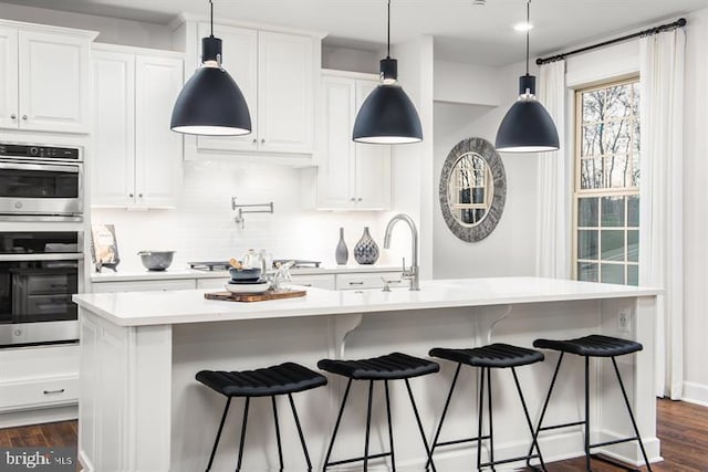 kitchen with white cabinetry, stainless steel appliances, dark hardwood / wood-style floors, and an island with sink