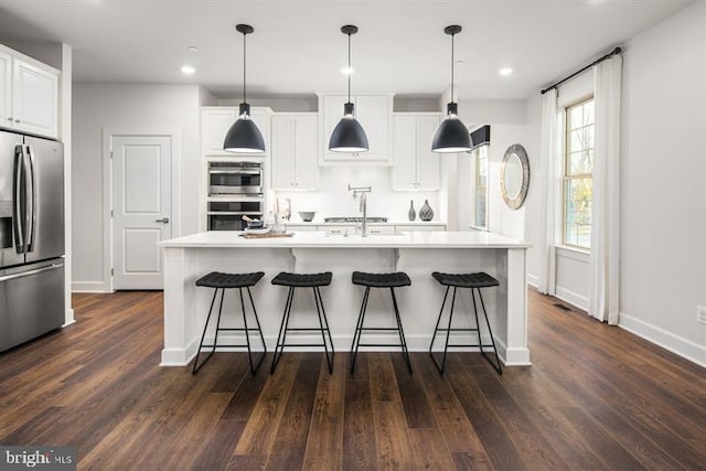 kitchen with white cabinetry, stainless steel appliances, decorative light fixtures, and a kitchen island with sink