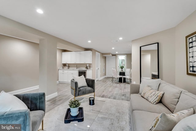 living area with baseboards, indoor wet bar, wine cooler, light wood finished floors, and recessed lighting