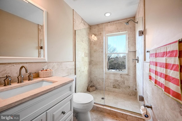 bathroom featuring tile patterned floors, toilet, tile walls, vanity, and a shower with door