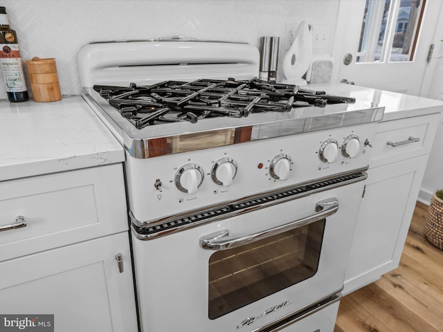 room details with white gas range oven, white cabinetry, backsplash, light stone counters, and light hardwood / wood-style floors