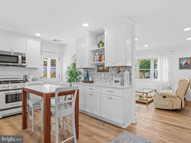 kitchen with backsplash, white gas range, light hardwood / wood-style floors, and white cabinets