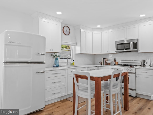 kitchen featuring sink, white cabinetry, fridge, white gas stove, and light wood-type flooring