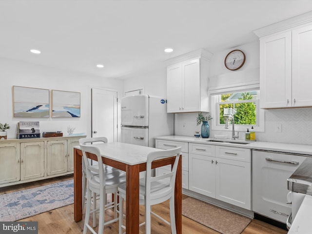 kitchen with white cabinetry, sink, backsplash, white appliances, and light hardwood / wood-style flooring