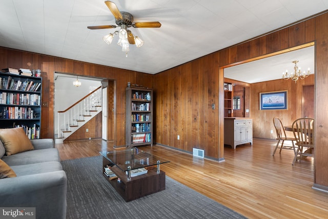 living room with hardwood / wood-style flooring, ceiling fan with notable chandelier, and wood walls