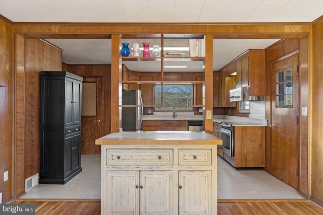 kitchen with extractor fan, sink, light hardwood / wood-style flooring, appliances with stainless steel finishes, and wooden walls